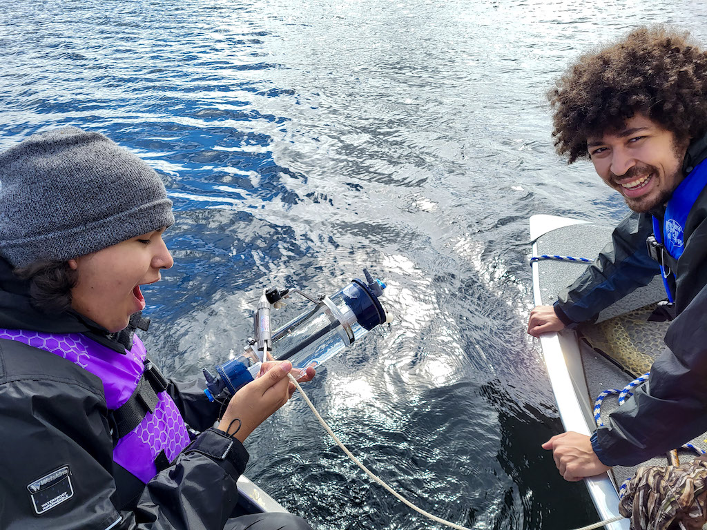 Two youth sampling water from a lake, part of Water First youth internship.