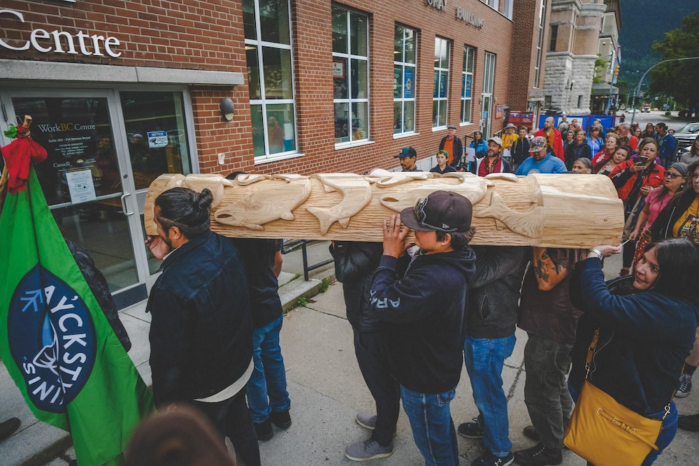 Sinixt people carrying a carved salmon pole into their new fish and wildlife office
