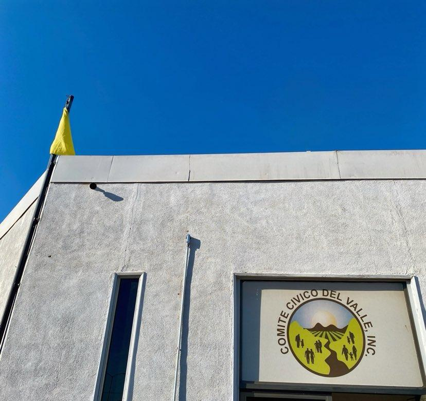 building front with Comite Civico Del Valle sign and yellow flag on pole